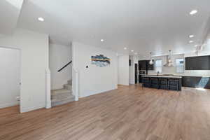 Unfurnished living room featuring recessed lighting, light wood-style flooring, and stairway