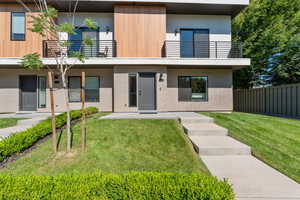 Contemporary home with brick siding, a front yard, a patio, stucco siding, and a balcony
