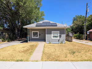 Bungalow-style home featuring solar panels, covered porch, and a front lawn