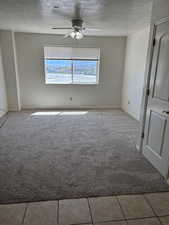 Unfurnished room featuring a textured ceiling, light carpet, ceiling fan, and light tile patterned flooring