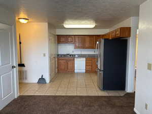 Kitchen with light tile patterned floors, freestanding refrigerator, brown cabinets, a textured ceiling, and white dishwasher