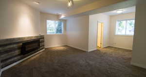 Additional living room area with dark colored carpet, healthy amount of natural light, and a glass covered fireplace