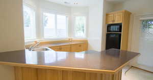 Downstairs wet bar area. Light brown cabinets, dark countertops, black appliances, and a peninsula