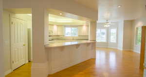 Kitchen featuring recessed lighting, light wood-style floors, white appliances, a ceiling fan, and a kitchen breakfast bar