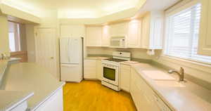 Kitchen featuring healthy amount of natural light, white appliances, light wood finished floors, and light stone countertops
