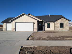 View of front of home with roof with shingles, stone siding, a garage, and concrete driveway