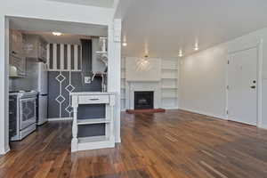 Kitchen with open shelves, electric range, dark wood finished floors, a fireplace with raised hearth, and freestanding refrigerator