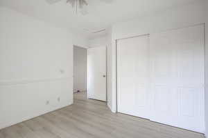 Unfurnished bedroom featuring attic access, light wood-style floors, a ceiling fan, and a closet