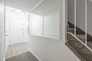 Corridor featuring light tile patterned floors, stairs, and light carpet