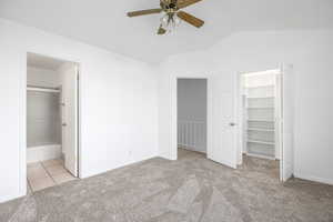 Unfurnished bedroom featuring a spacious closet, light colored carpet, ensuite bath, lofted ceiling, and a ceiling fan