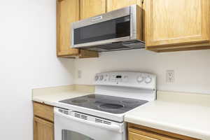 Kitchen with white electric stove, stainless steel microwave, and light countertops
