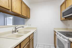 Kitchen with brown cabinetry, light countertops, white appliances, and light tile patterned floors