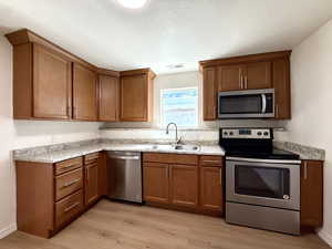 Kitchen featuring appliances with stainless steel finishes, brown cabinetry, light wood finished floors, and a textured ceiling