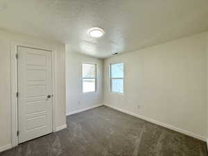Unfurnished room featuring a textured ceiling and dark carpet