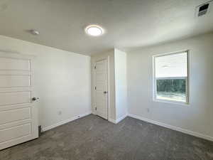 Unfurnished bedroom with dark carpet and a textured ceiling