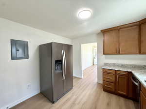 Kitchen with appliances with stainless steel finishes, light wood-style floors, electric panel, brown cabinets, and a textured ceiling