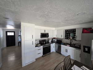 Kitchen featuring dark countertops, appliances with stainless steel finishes, light wood-style flooring, white cabinets, and decorative backsplash