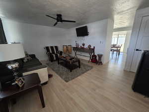 Living room featuring a textured ceiling, light wood finished floors, and a ceiling fan