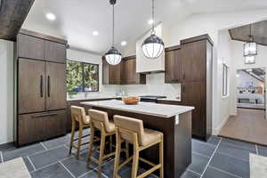 Kitchen with a kitchen bar, a center island, hanging light fixtures, paneled built in refrigerator, and dark brown cabinets