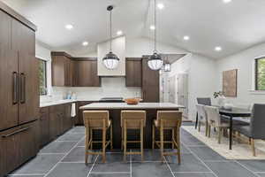 Kitchen featuring hanging light fixtures, a center island, vaulted ceiling, paneled refrigerator, and a kitchen bar