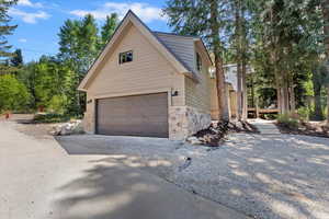 View of side of home with stone siding, an attached garage, and driveway