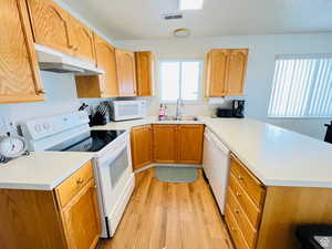 Kitchen featuring white appliances, a peninsula, light wood finished floors, and light countertops