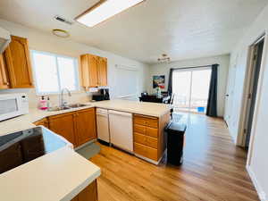 Kitchen with light wood-style flooring, a peninsula, brown cabinetry, light countertops, and a textured ceiling