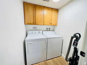 Laundry area with light wood-style floors, cabinet space, and washer and clothes dryer