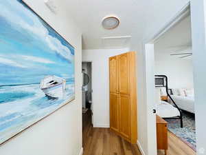 Corridor with a textured ceiling, light wood finished floors, and attic access