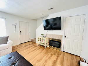 Living area featuring a stone fireplace, a textured ceiling, and light wood-style flooring