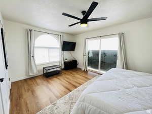 Bedroom with a textured ceiling, access to exterior, light wood finished floors, and ceiling fan