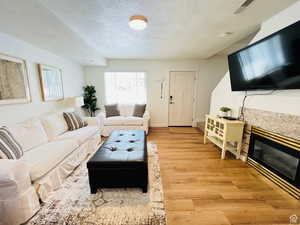 Living area with a textured ceiling, a tiled fireplace, and light wood finished floors