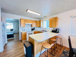 Kitchen featuring light countertops, light wood-style floors, white appliances, a textured ceiling, and a breakfast bar area