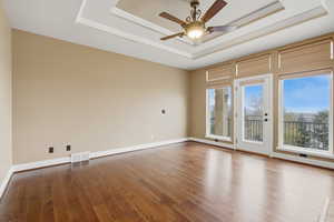 Empty room featuring hardwood / wood-style floors, a ceiling fan, and a raised ceiling