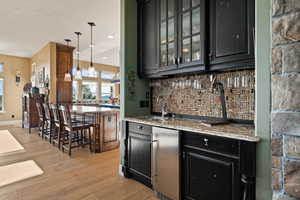 Indoor wet bar featuring decorative backsplash, light wood-style floors, recessed lighting, and pendant lighting