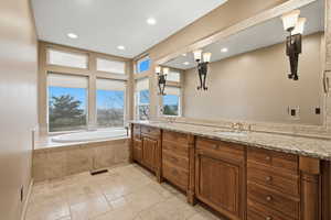 Full bath with double vanity, stone tile flooring, a garden tub, and recessed lighting