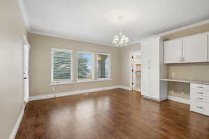 Unfurnished dining area featuring built in study area, ornamental molding, dark wood-style floors, and a chandelier