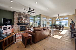 Living area featuring light wood-type flooring, a ceiling fan, a fireplace, recessed lighting, and a chandelier