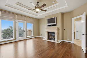 Unfurnished living room with ceiling fan, hardwood / wood-style floors, a tray ceiling, a fireplace, and ornamental molding