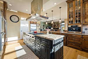 Kitchen featuring island range hood, light wood-style flooring, a center island with sink, glass insert cabinets, and recessed lighting
