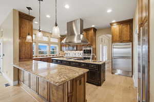 Kitchen featuring arched walkways, pendant lighting, stainless steel appliances, light stone counters, and light wood-style floors