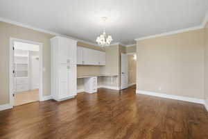 Unfurnished dining area featuring built in desk, dark wood-style floors, crown molding, and a chandelier