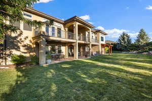 Rear view of house featuring stucco siding, a patio, a lawn, and a balcony
