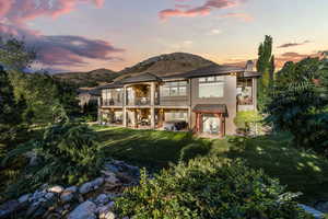 Back of house at dusk with a patio, a lawn, a balcony, a chimney, and stucco siding