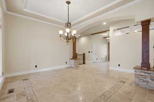 Spare room with stone tile flooring, crown molding, a raised ceiling, a chandelier, and inlaid floor details