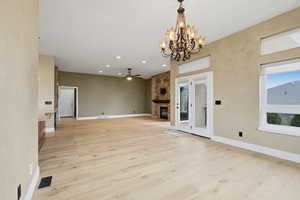 Unfurnished living room with a fireplace, ceiling fan, recessed lighting, light wood-style flooring, and a chandelier
