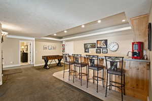 Indoor wet bar with carpet, a textured ceiling, recessed lighting, and a raised ceiling