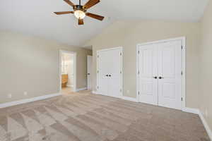 Unfurnished bedroom featuring multiple closets, carpet floors, lofted ceiling, ensuite bath, and a ceiling fan