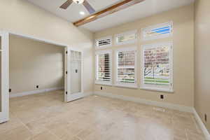 Spare room featuring beamed ceiling, light stone finish floors, ceiling fan, and french doors