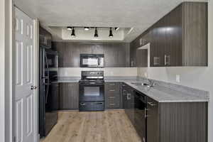 Kitchen featuring modern cabinets, black appliances, light granite counters, and light wood-type flooring